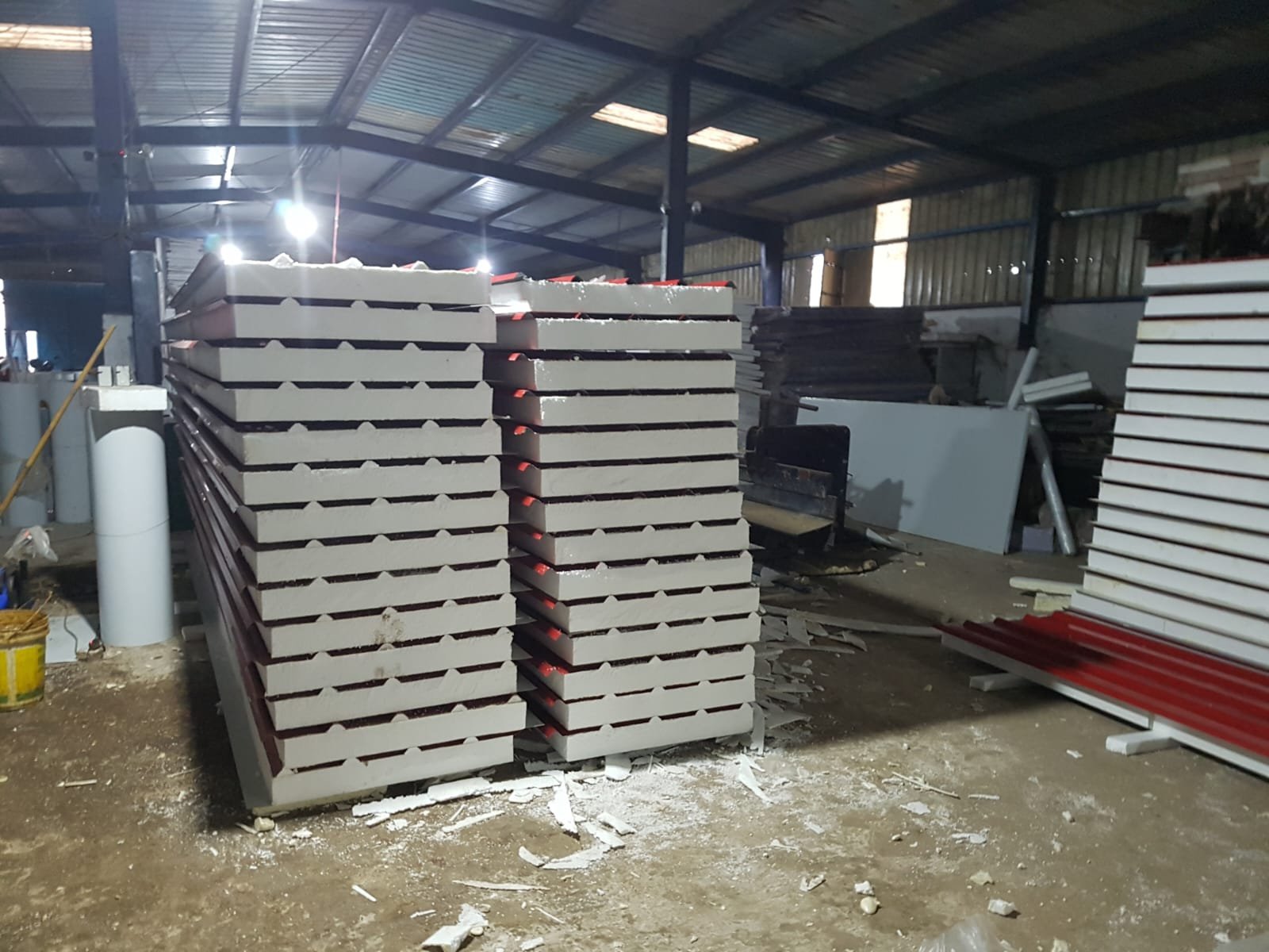 Two tall stacks of white ribbed insulated roof panels with red undersides on a factory floor